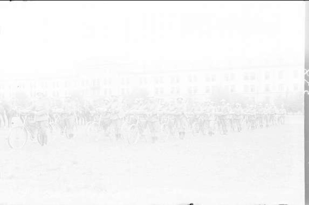 Schwarzes und weißes Foto von Radfahrern, die im Schnee an einem Gebäude vorbeifahren.