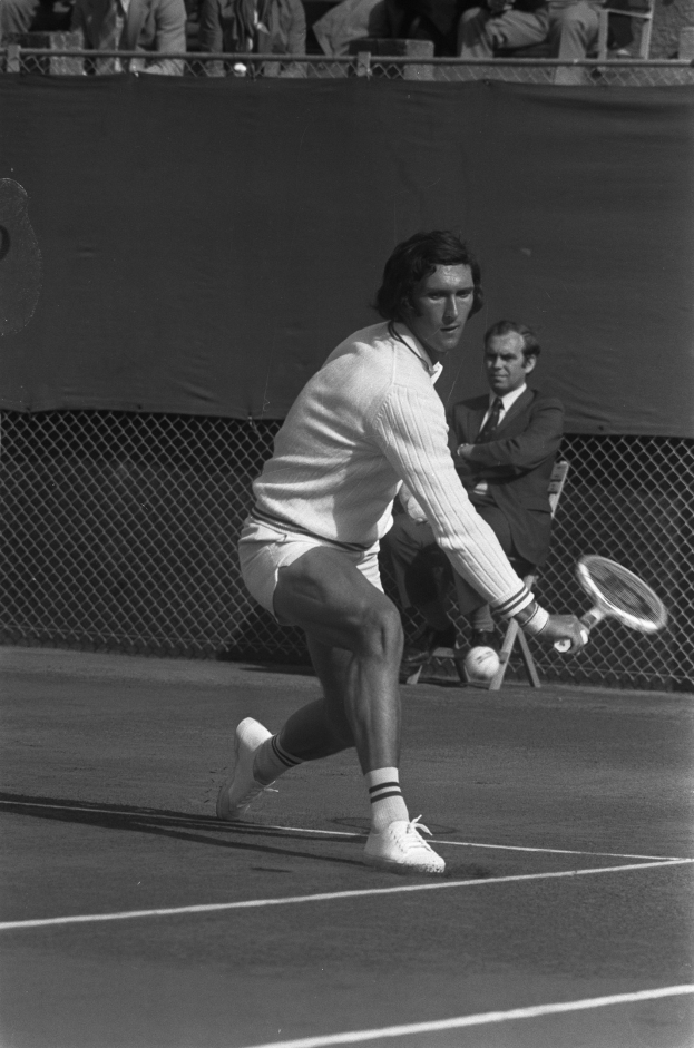 Ein professioneller Tennisspieler schlägt mit einem Schläger nach einem Ball auf einem Court mit Maschendrahtzaun und Zuschauern im Hintergrund.