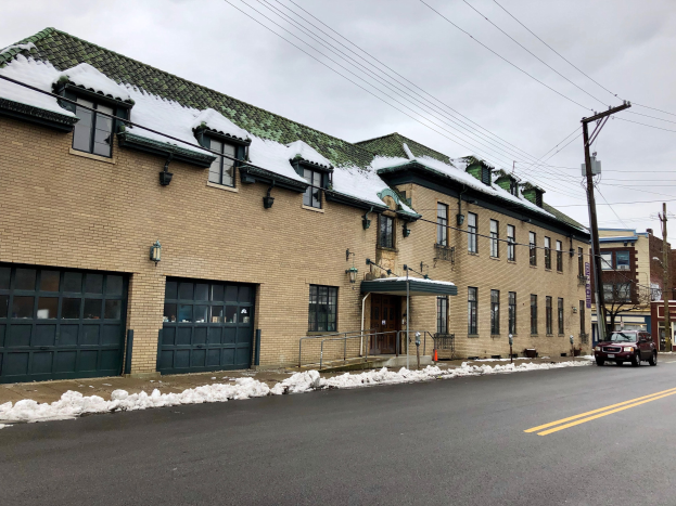 Großes Backsteingebäude mit grüner Dachfläche an einer Straßenkreuzung, als ehemalige Feuerwache St. Louis bezeichnet, umgeben von Fahrzeugen, Schnee, Strommasten, Bäumen und einem bewölkten Himmel.