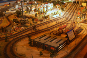 Eine detaillierte Modellbahnausstellung in einem Museum, die Gebäude, Bäume, Schienen, Fahrzeuge, Pfosten, Lampen und Platten umfasst, die eine belebte Stadtlandschaft nachahmen.