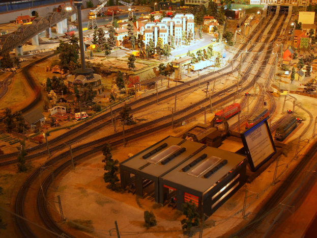 Eine detaillierte Modellbahnausstellung in einem Museum, die Gebäude, Bäume, Schienen, Fahrzeuge, Pfosten, Lampen und Platten umfasst, die eine belebte Stadtlandschaft nachahmen.