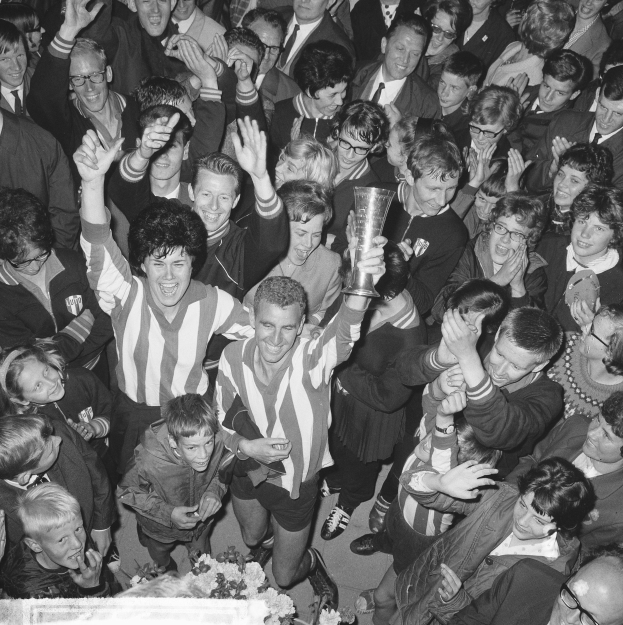 Schwarzes Bild einer Gruppe von Menschen, die mit einem Pokal feiern, der zentrale Figur hält den Becher, umgeben von einer Menge, mit Blumen unten.