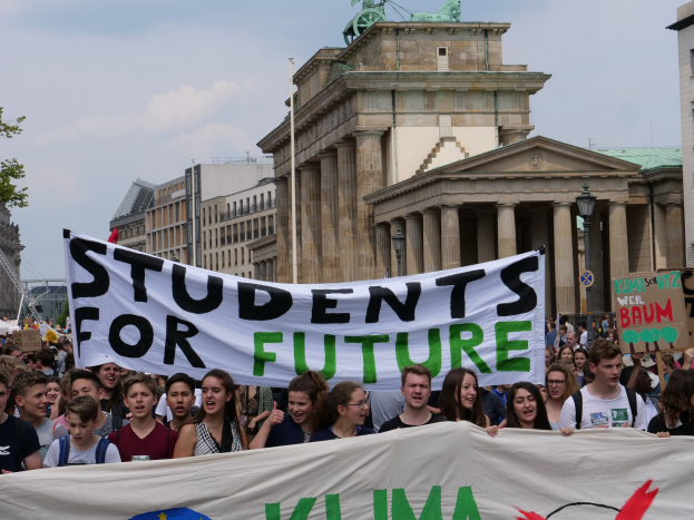 Eine Gruppe von Schülern marschiert in Berlin mit einer bunten "Students for Future"-Schlagzeile gegen eine Kulisse aus Geb├Ąuden, B├Ąumen und Himmel.