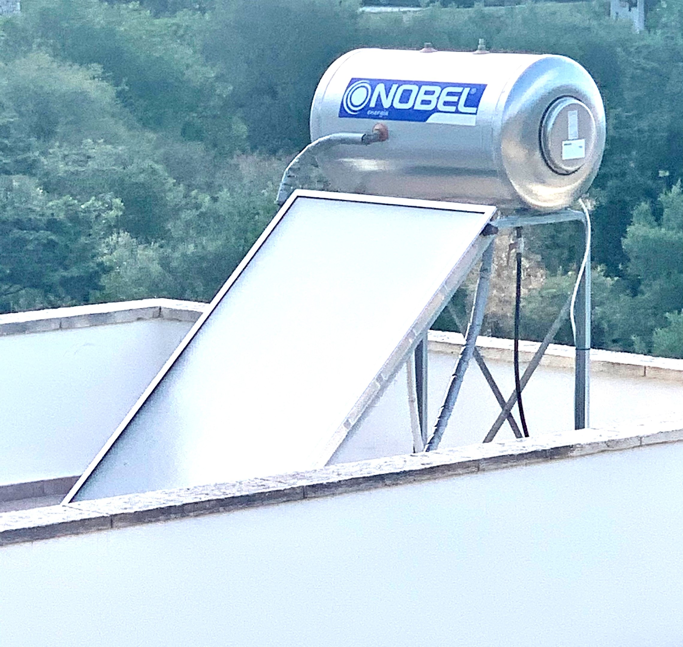 Solarwassererhitzer mit einem Speicherbehälter, der auf dem Dach eines Gebäudes montiert ist, mit Bäumen im Hintergrund.