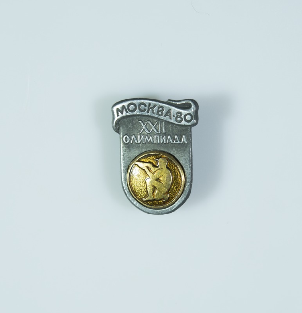 Eine Silber- und Goldnadel mit einem Männerbildnis, die das 80-jährige Jubiläum der Olympischen Spiele in Moskau feiert, mit einer Inschrift darauf.