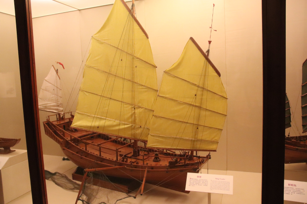 Holzmodellsegelschiff in einer Glasvitrine mit Informationsschildern im Hintergrund.