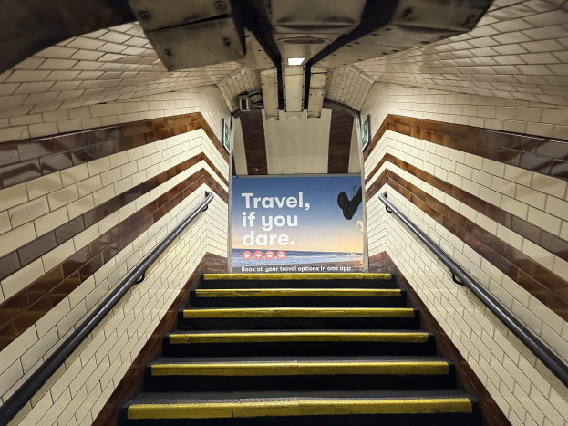 Eine Treppe in einer U-Bahn-Station mit einem Schild, das 'Reise, wenn du wagst' oben trägt, flankiert von Geländern und sichtbaren Stationswänden.