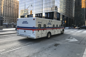 Ambulanz auf einer Stadtstraße mit hohen Gebäuden, Straßenmöbeln und Passanten geparkt, unter einem sichtbaren Himmel.