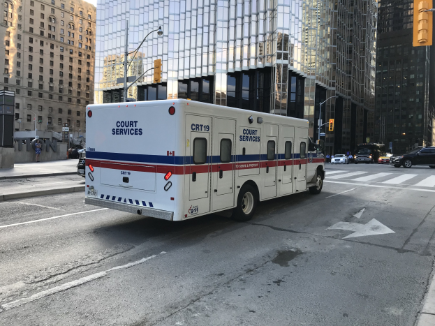Ambulanz auf einer Stadtstraße mit hohen Gebäuden, Straßenmöbeln und Passanten geparkt, unter einem sichtbaren Himmel.