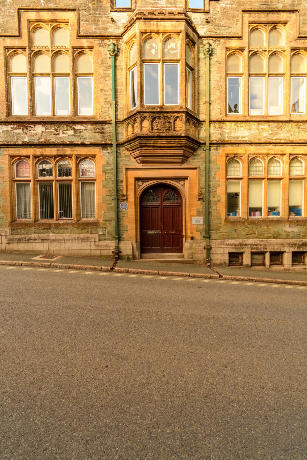 Alter Bau mit vielen Fenstern und einer hölzernen Tür an der Seite einer Straße, mit Rohren an seinen Wänden.