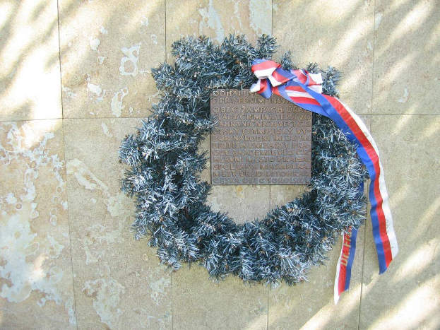 Ein Kranz mit einer rot-weiß-blauen Schleife an einer Gebäudewand, wahrscheinlich ein Denkmal für Kriegsopfer.