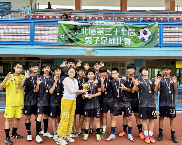 Junge Männer in Fußballtrikots stehen auf einem Feld und halten einen Pokal, während sie Medaillen tragen und ein Banner für die 'Yokohama U-16 Jungenfußballmannschaft' im Hintergrund zu sehen ist.