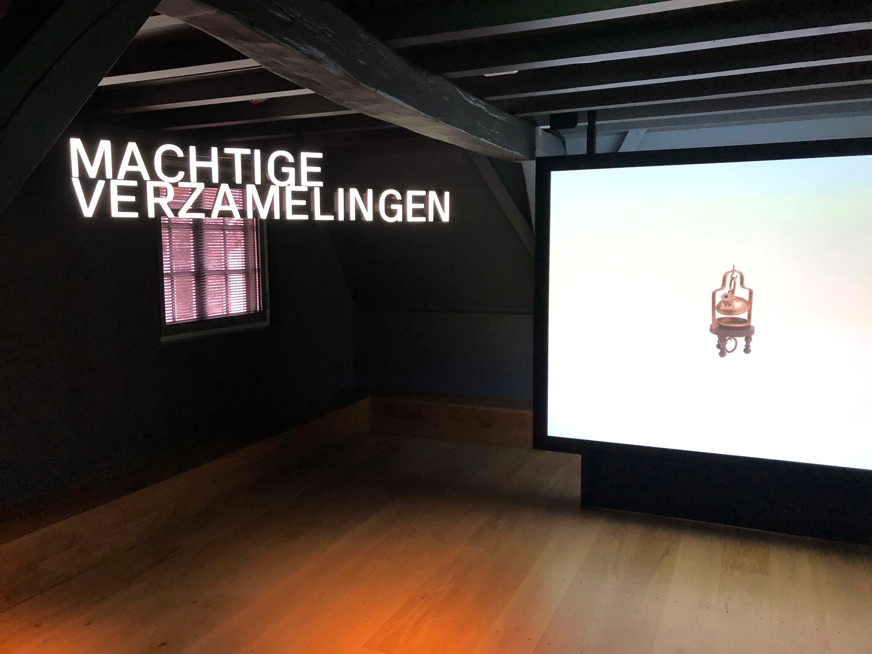 Installationsansicht der Ausstellung 'Machtige Sammlung' im Museum of Modern Art in Berlin, mit einem großen Bildschirm mit Wandtext, einem Fenster links und der Decke oben.