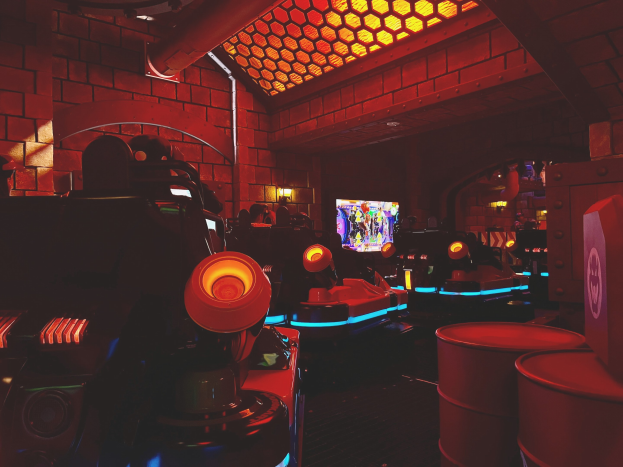 Ein hell erleuchteter Arcade-Raum voller verschiedener Videospielautomaten, Bildschirme und Gegenstände, darunter eine sichtbare Röhre und Deckenleuchten.