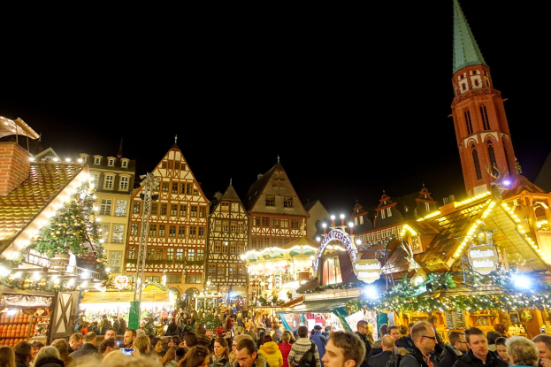 Ein geschäftiger Weihnachtsmarkt in Nürnberg, Deutschland mit Menschen um geschmückte Stände, festliche Lichter, Gebäude mit Fenstern, ein Uhrenturm und einen dunklen Himmel.