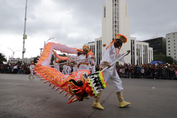 Eine Gruppe von Menschen in Kostümen führt einen Drachen Tanz mit Stöcken vor einer Menge während der chinesischen Neujahrsfeier in Brisbane durch, mit Gebäuden, Bäumen und Laternenmasten im Hintergrund.