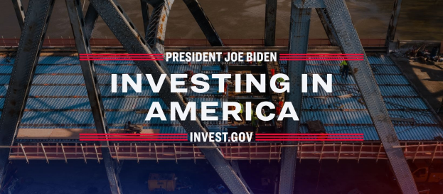 Präsident Joe Biden mit einer Brücke im Hintergrund, verschiedenen Gegenständen am Boden und dem Text "In America investieren" in der Mitte.