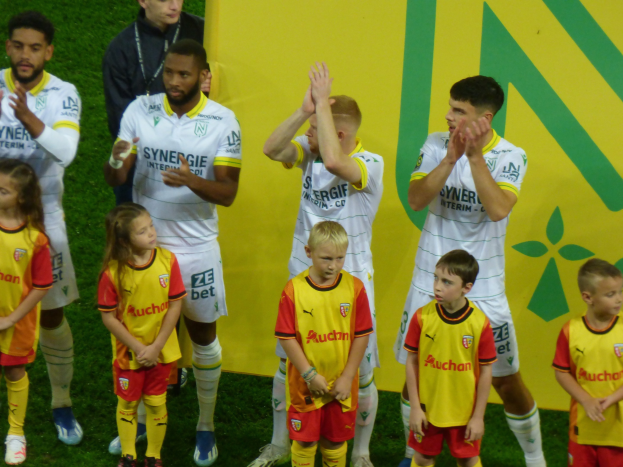 Eine Gruppe junger Fußballspieler in Uniformen, die auf einem Feld klatschen, mit einem 'Ligue 1'-Schild im Hintergrund, feiern einen Sieg.