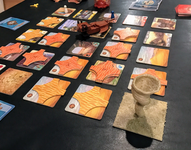 Ein Tisch voller Star Wars: The Old Republic-Brettspielkarten, -figuren und anderen Gegenständen in einem Raum mit einer Wand im Hintergrund.