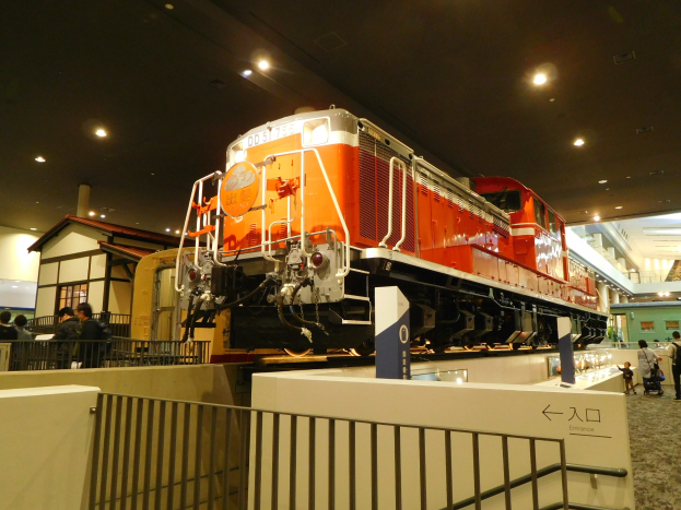 Roter und weißer Zug auf Museumsdiorama umgeben von Besuchern und Informationsschildern.