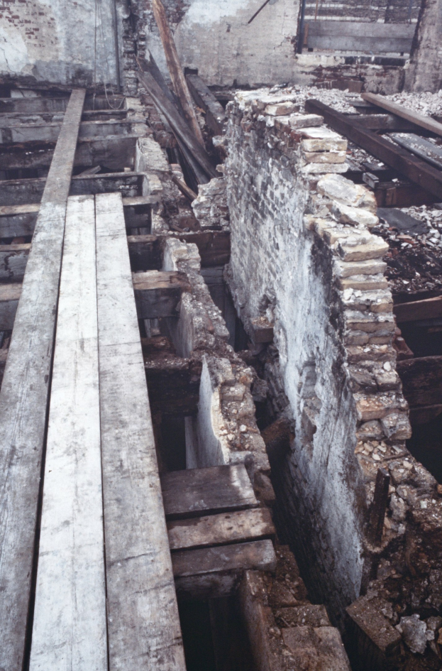 Altbau im Abrissprozess mit verstreuten Holzplanken und Steinen im Vordergrund und einer remaining Wand im Hintergrund.