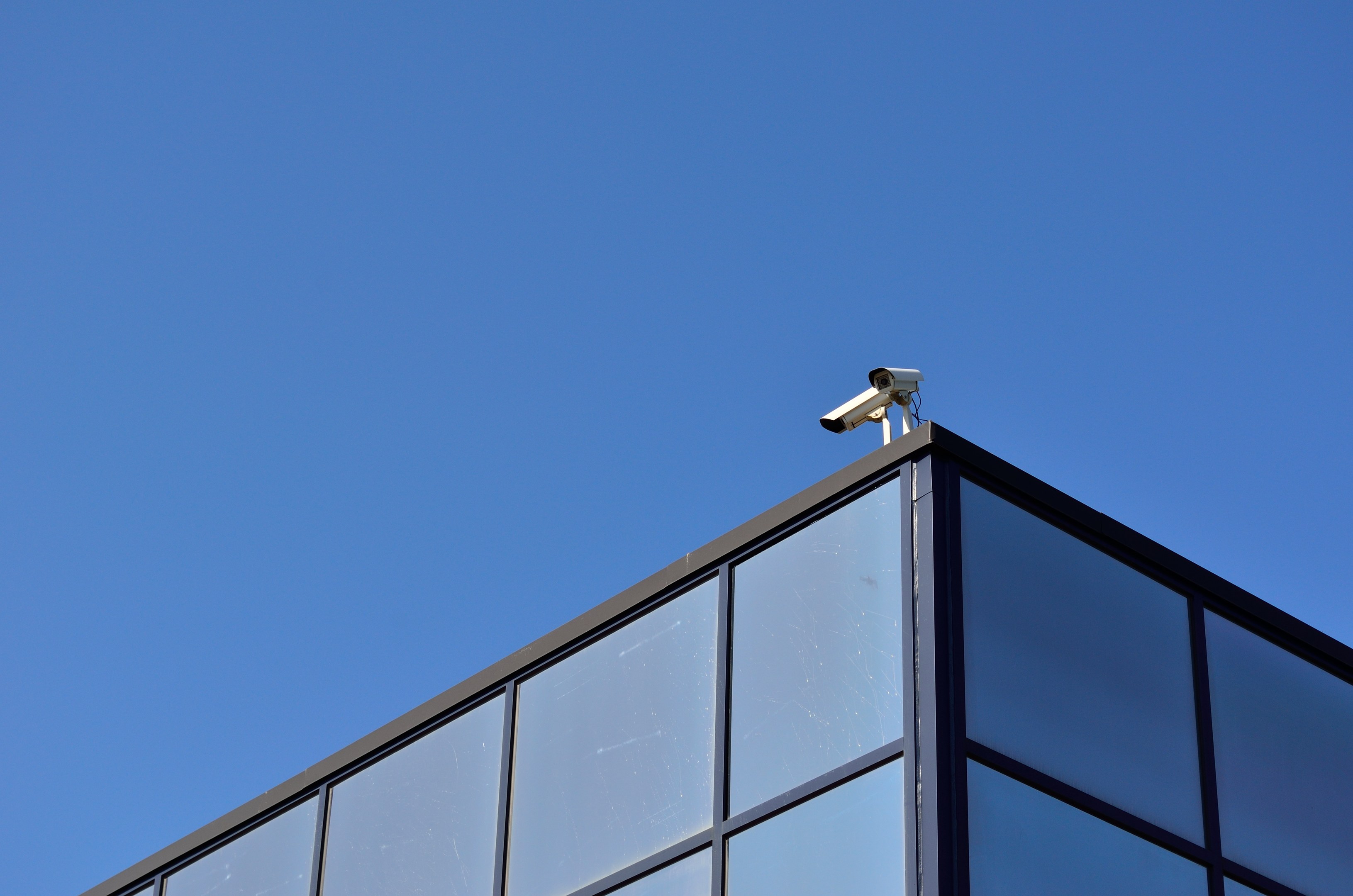 Sicherheitskamera an der Seite eines Gebäudes unter einem klaren blauen Himmel.
