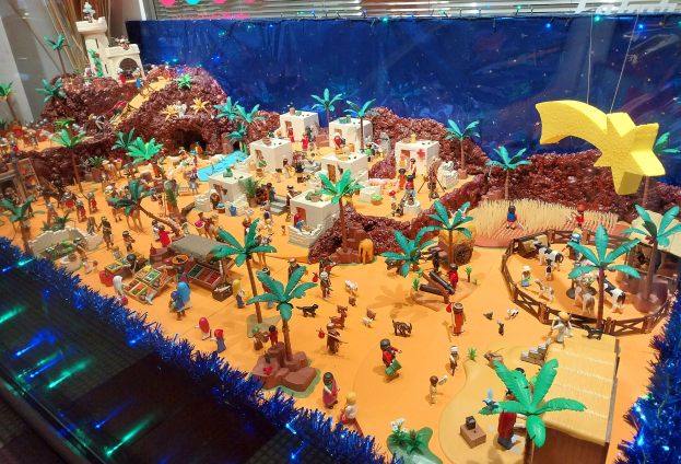 Ein Vitrine voller verschiedener Lego-Steine und Sets auf einem Tisch, umgeben von Spielzeugen und dekorativen Elementen, mit einer beleuchteten Wand im Hintergrund.