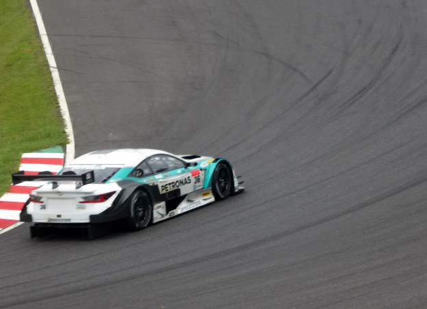 Ein silberner Mercedes-AMG GT3-Rennwagen mit Werbetext auf der Karosserie, der auf einer Rennstrecke fährt, mit Gras auf der linken Seite sichtbar.