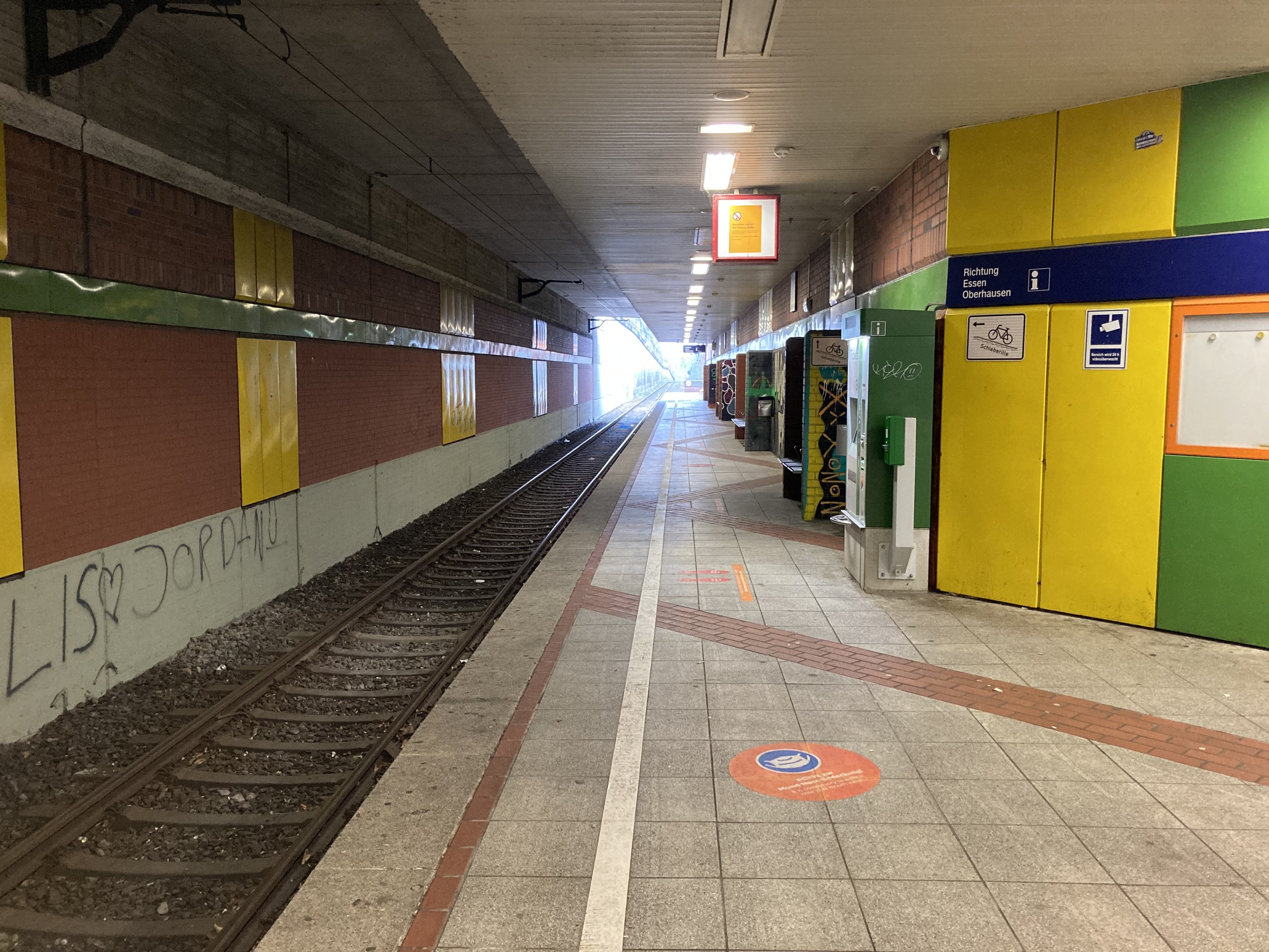 Ein Bahnsteig in Berlin Hauptbahnhof, Deutschland, mit einem Zug auf den Schienen, beleuchtet von Deckenlampen, mit Graffiti an der linken Wand und ein paar Gegenständen auf der rechten Seite.