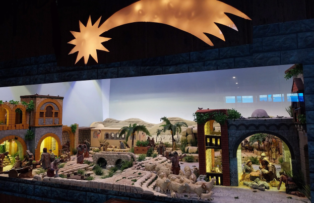 Eine Krippe in einem Museum mit Figuren, Tieren, Häusern und Pflanzen, beleuchtet von einer Deckenbeleuchtung an der Wand.