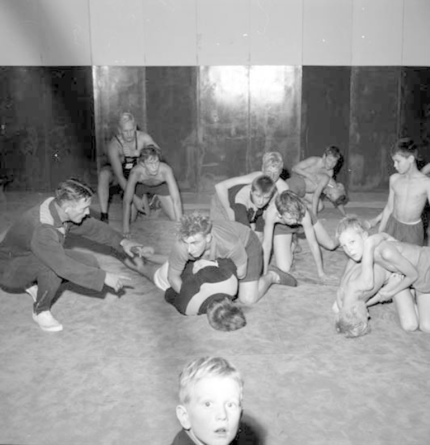 Schwarz-weißes Bild von jungen Jungs, die in einem Gym kämpfen, mit einer Wand im Hintergrund.