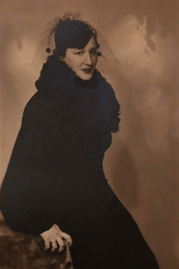 Ein Schwarz-Weiß-Porträt von Mary Elizabeth Taylor in einem 1920er-stilschwarzen Kleid und Schleier, sitzend mit einem warmen Ausdruck und dezenter Make-up, vor einem sanft unscharfen Hintergrund.