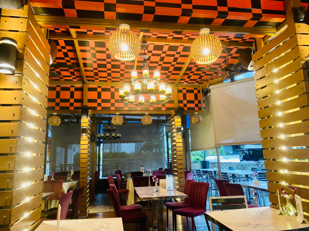 Ein Restaurant-Innenraum mit Tischen und Stühlen unter einer karierten Decke, geschmückt mit Blumenvasen und anderen Dekorationen, mit Wänden, die mit Leuchten und Kronleuchtern verziert sind.