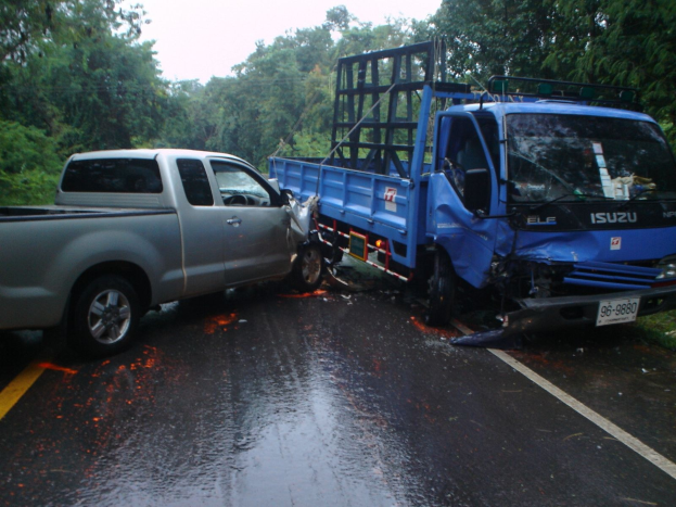 Ein geschädigter Lkw mit eingedrückter Front und verbeulter Karosserie steht abseits der Straße, umgeben von Bäumen unter einem klaren blauen Himmel.