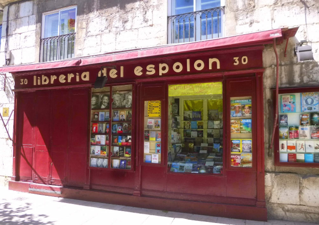 Ein zweistöckiges Gebäude mit einer Schaufensterfront, die ein rotes Vordach trägt, auf dem 'Libreria del Espolon' steht und ordentlich aufgereihte Bücher im Inneren zeigt.