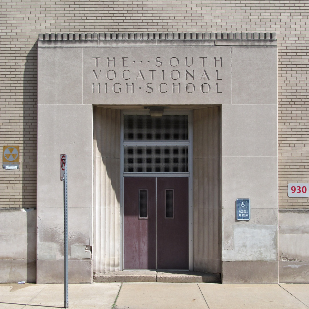 Das Südbildungshaus mit einer Tür, Schilder an der Wand und einem Weg, der zur Einfahrt führt.