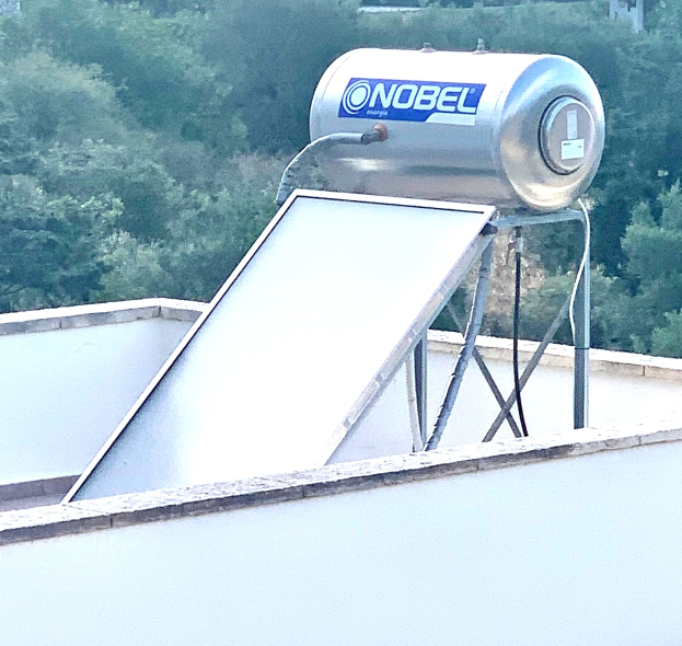 Solarwassererwärmer mit Speicher auf einem Gebäude installiert, Bäume im Hintergrund sichtbar.