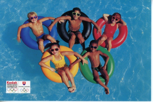 Fünf Kinder mit Schwimmbrillen sitzen auf aufblasbaren Reifen in einem klaren Schwimmbad mit sichtbarem Text und Logos auf der linken Seite.