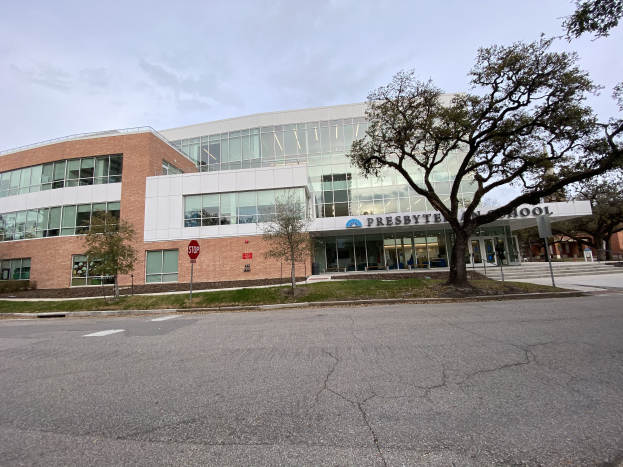 Presbyter Middle School, ein großes Gebäude mit zahlreichen Fenstern, umgeben von Bäumen, Gras, Schildern, Pfosten und einer Straße, mit einem bewölkten Himmel im Hintergrund.