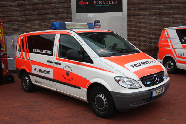 Zwei Rettungswagen nebeneinander vor einem Gebäude mit einer Wand im Hintergrund, einem Feuerlöscher und anderen Gegenständen auf der linken Seite.