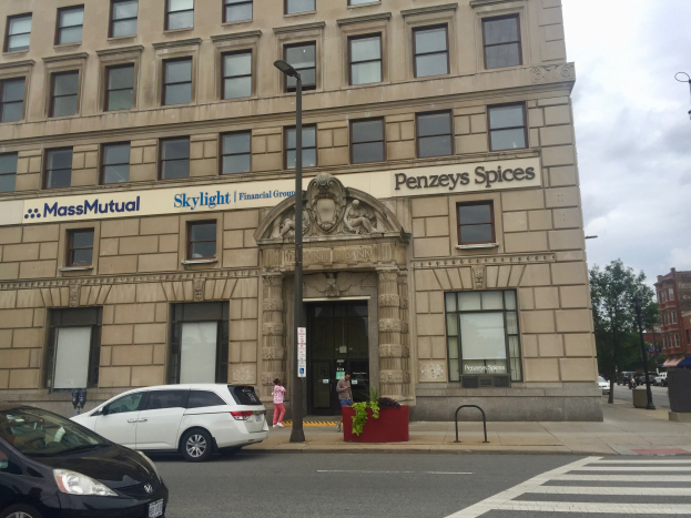 Großes Gebäude mit parkenden Autos, Straßenlaternen, Fahrzeugen, Fußgängern, Grünfläche und bewölktem Himmel, identifiziert als Hauptsitz der Massachusetts Mutual Financial Group.