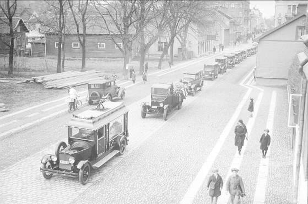 Schwarze und weiße Straßenszene in Berlin aus den 1930er-1940er Jahren, die Autos, Fußgänger, Gebäude, Bäume und einen klaren Himmel zeigt.