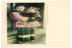 Eine alte Postkarte mit einer Frau, die ein Baby im Arm hält und beide fröhlich in die Kamera schauen, mit einer Inschrift, die wahrscheinlich 'Frohes neues Jahr' wünscht.