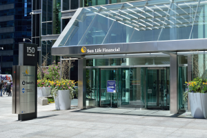Moderner Glaswand-Sun Life Financial-Gebäude in Toronto mit einer Hinweistafel, Topfpflanzen mit Blüten, Fußgängern, einer Straßenlaterne, einem Schild, Fahrzeugen und einer bewölkten Himmel.