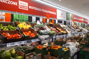 Eine Ladeneinrichtung mit verschiedenen Obst- und Gemüsesorten in Kartonschachteln mit Preisschildern, die informative Schilder an den Wänden und Deckenbeleuchtung zeigen.