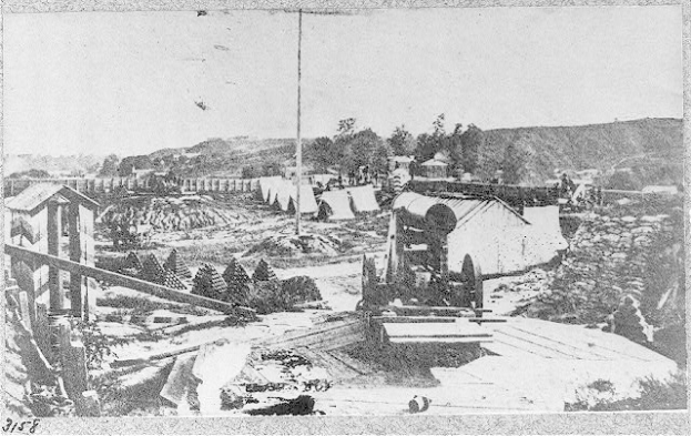 Ein Schwarz-Weiß-Foto einer Baustelle in San Francisco, Kalifornien, mit einer Maschine im Vordergrund, umgeben von Hütten, Bäumen, Hügeln und einem Himmel im Hintergrund, mit Text unten, der besagt: "Die Baustelle einer neuen Brücke in der Stadt San Francisco, Kalifornien."