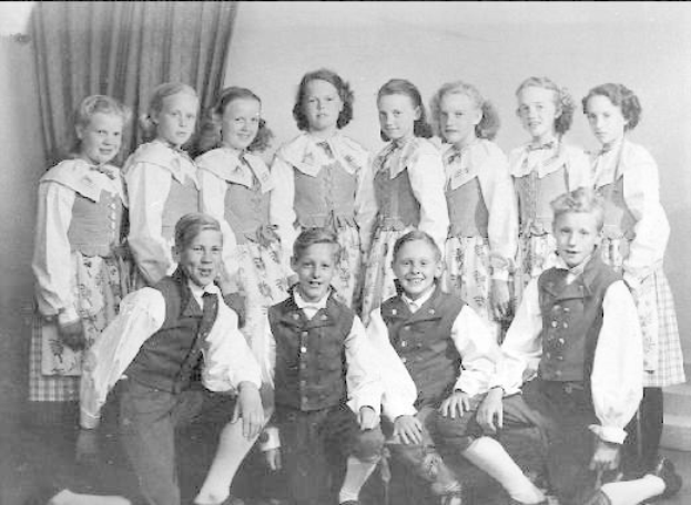 Schwarzes und weißes Foto einer Gruppe von Kindern, die vor einer Wand mit einem Vorhang posieren, beschriftet mit "1930er Kinder Schule" unten.