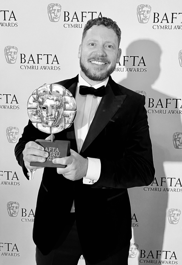 Ein Mann in einem Smoking, der eine BAFTA-Trophäe hält und lächelt, vor dem Hintergrund 'BAFTA Awards 2018.'