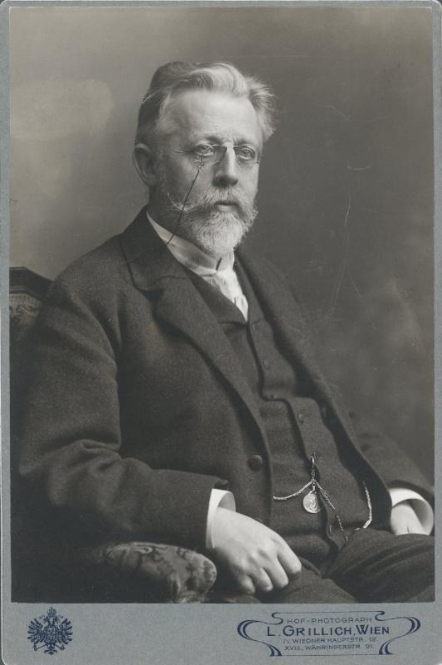 Schwarzes und weißes Porträt eines bärtigen Mannes mit Brille, der in einem Stuhl sitzt, mit Text unten, der lautet "L. Grillich Wien, der Gründer der deutschen Revolution".