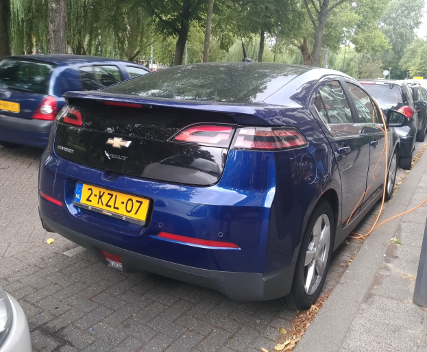 Elektroauto an einer Ladestation auf einer Straße mit Bäumen unter einem klaren blauen Himmel